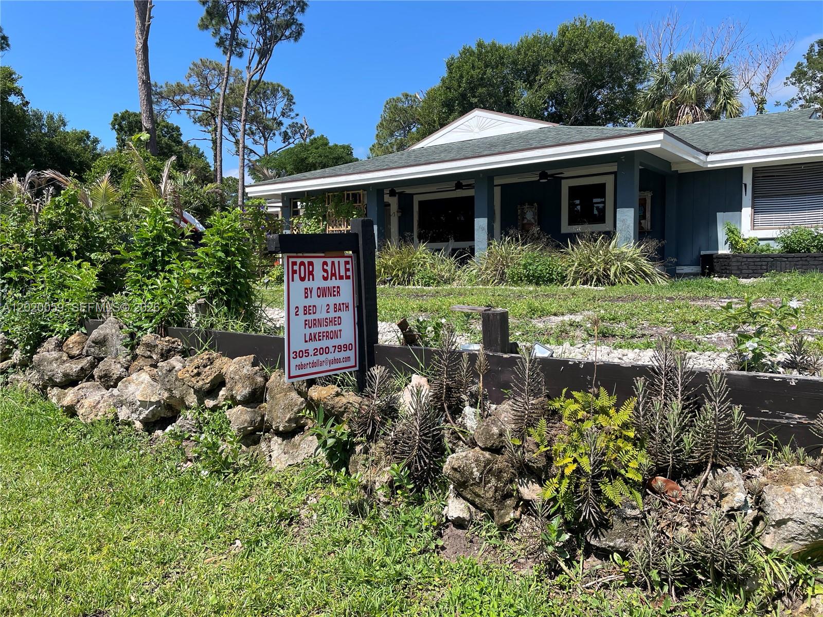 A blue house with a for sale sign stands behind a rock wall and landscaping — 6703 Oneco Way, Fort Pierce FL 34951, FORT PIERCE, FL
