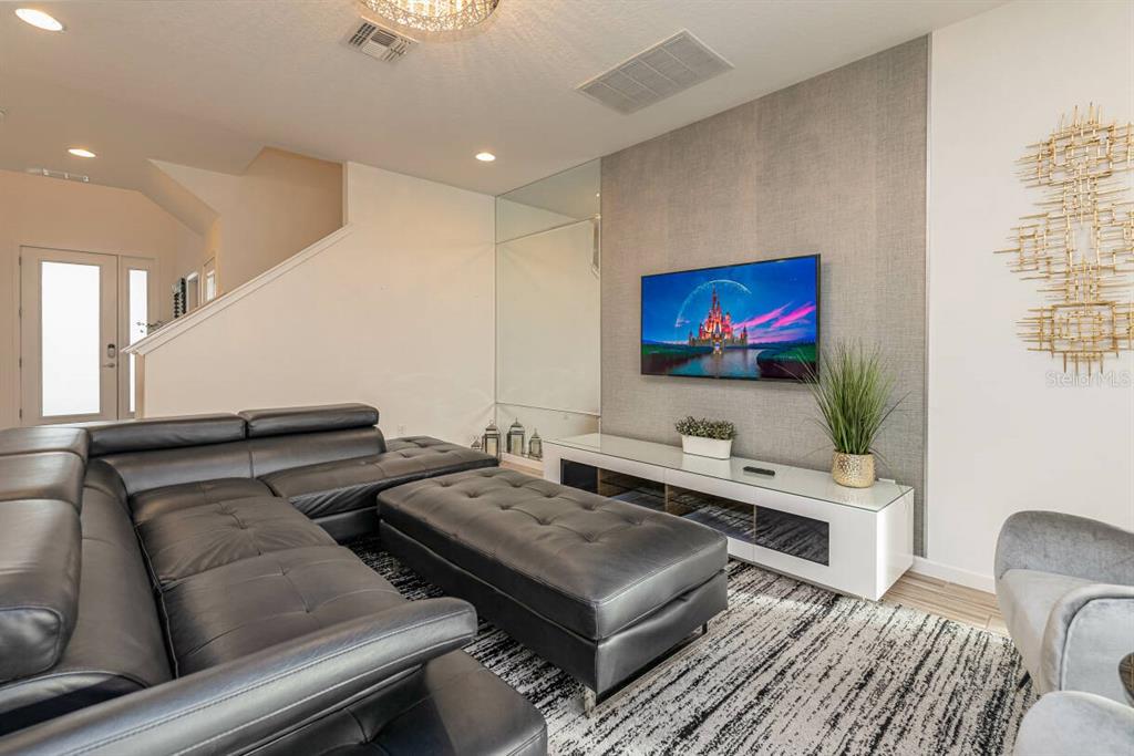 A modern living room features a black leather sectional, a wall-mounted television, and mirrored accents — 2678 CALISTOGA AVENUE, KISSIMMEE, FL