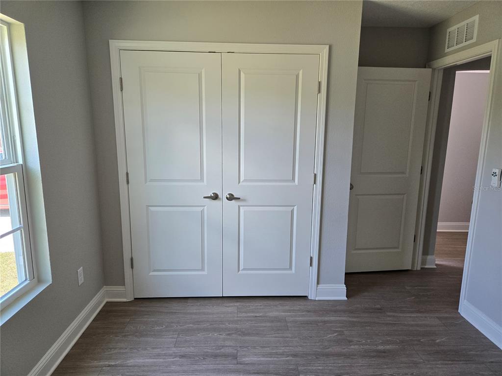 A room features light gray walls, wood-look flooring, a window, and two sets of white doors — 4437 BESSIE CIRCLE E, JACKSONVILLE, FL