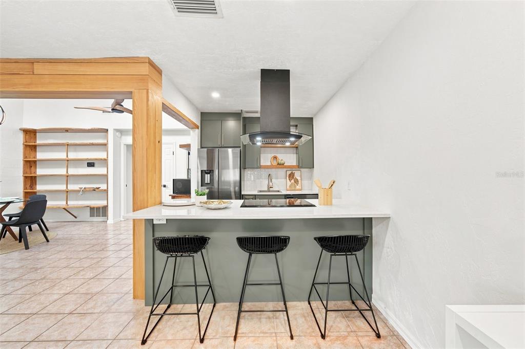 A kitchen features a white island with three black stools and dark green cabinetry — 747 SE 2ND PLACE UNIT 2, GAINESVILLE, FL