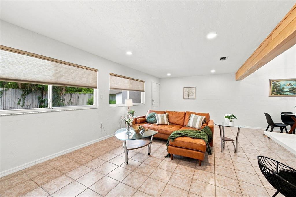 A living room features a brown leather sectional, tile flooring, and two windows with shades — 747 SE 2ND PLACE UNIT 2, GAINESVILLE, FL