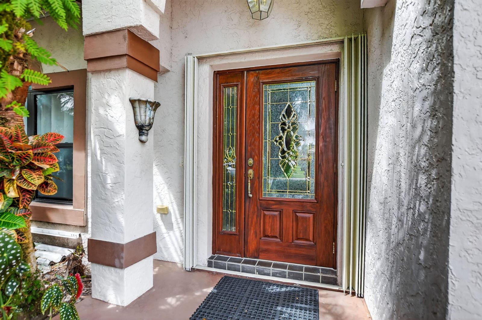 A wooden front door with a decorative glass insert and sidelight sits under a porch — 20174 Back Nine Drive, Boca Raton FL 33498, BOCA RATON, FL