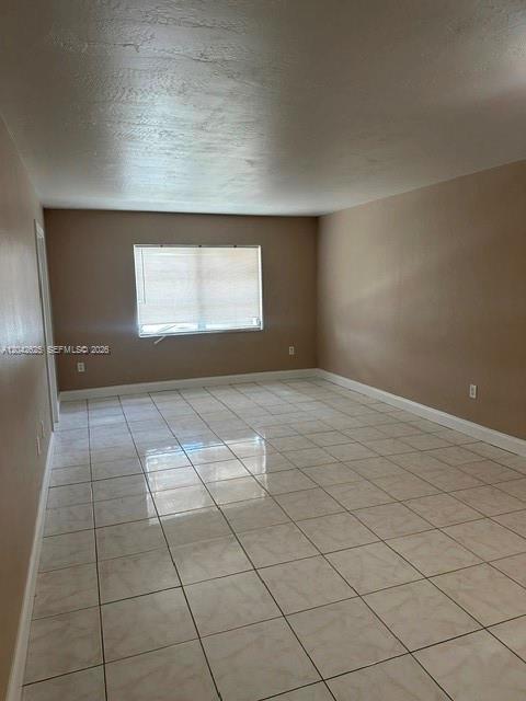 An empty room features light-colored tile flooring, beige walls, and a single window with blinds — 251 NE 187th St # 809, Miami FL 33179, MIAMI, FL