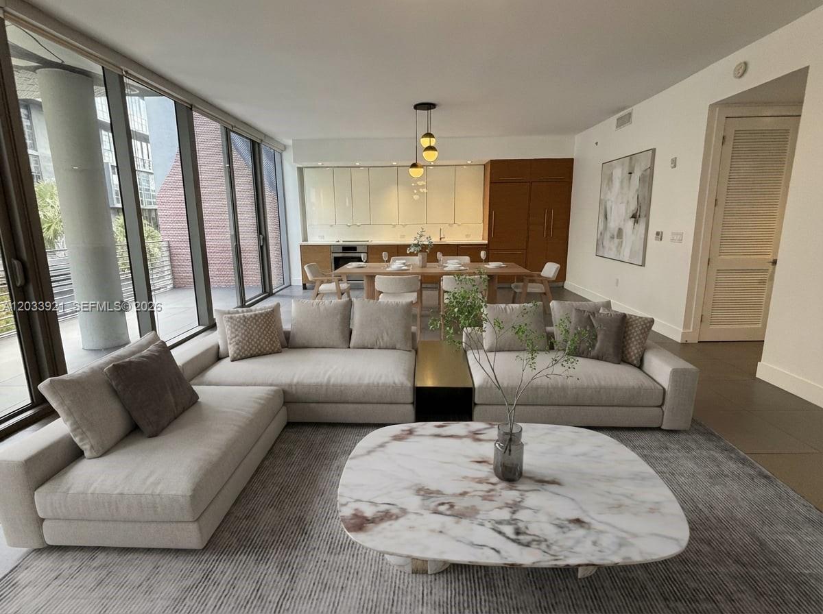 A modern living room features a large sectional sofa, marble coffee table, and adjacent dining area — 250 NW 24th St # 3C, Miami FL 33127, MIAMI, FL