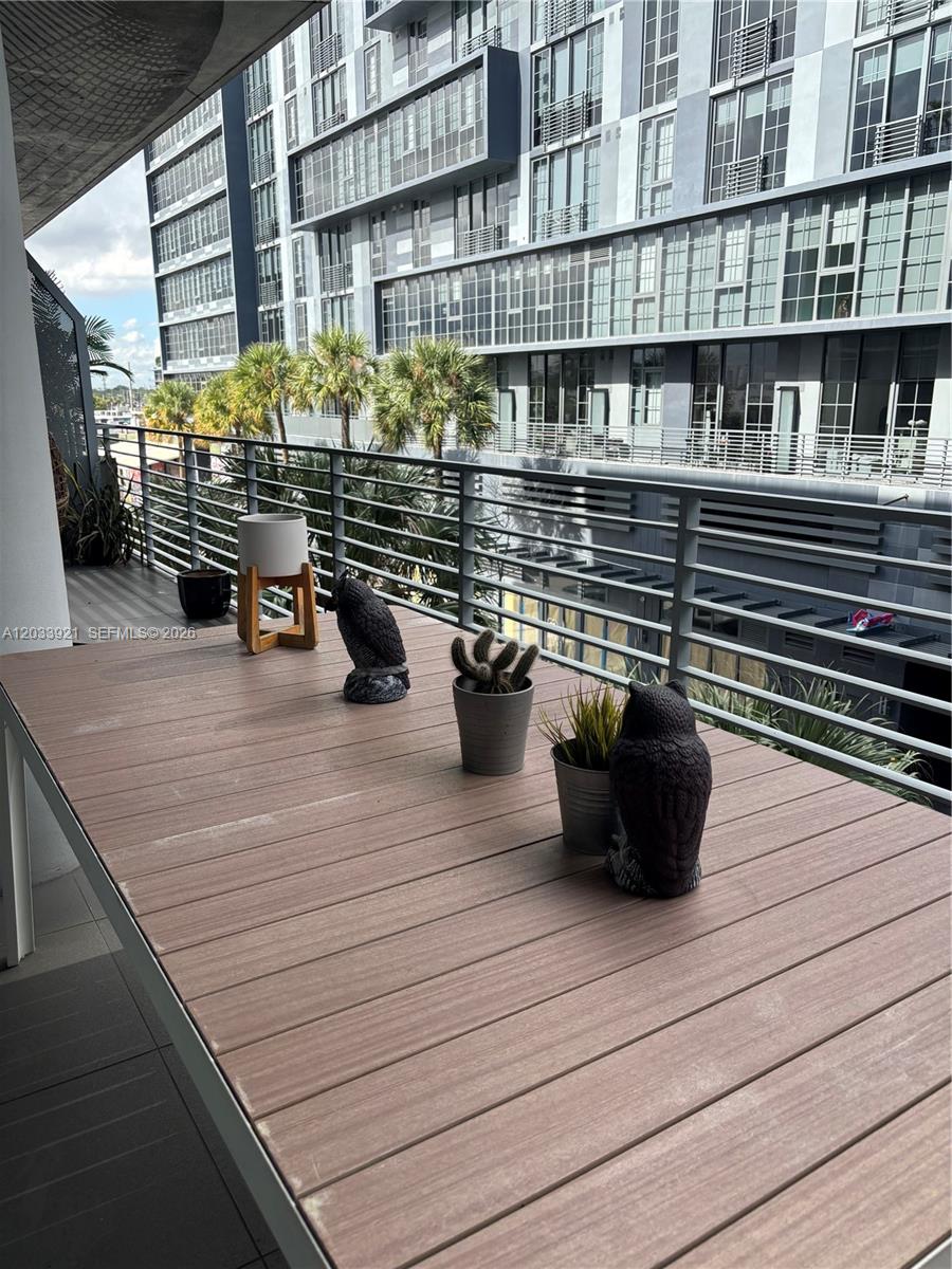 A balcony features a wooden table with potted plants and owl figurines overlooking a building — 250 NW 24th St # 3C, Miami FL 33127, MIAMI, FL