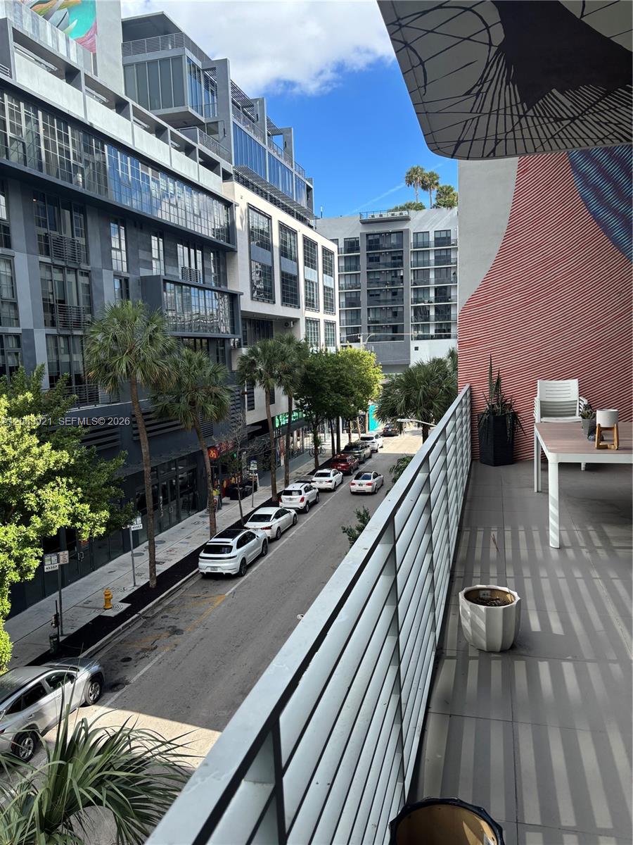 A balcony with a table and chairs overlooks a city street lined with parked cars — 250 NW 24th St # 3C, Miami FL 33127, MIAMI, FL