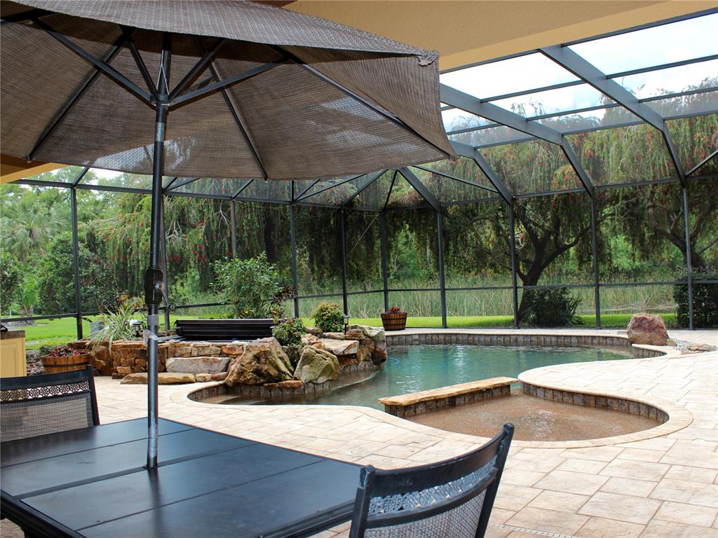 A covered patio features a swimming pool, a hot tub, and a large outdoor umbrella — 406 PETREL TRAIL, BRADENTON, FL