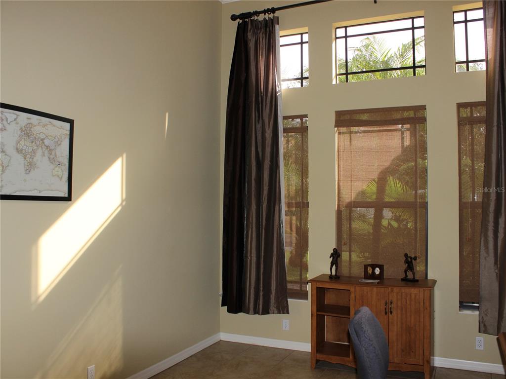 A room with high ceilings, tall windows with brown curtains, and a wooden cabinet — 406 PETREL TRAIL, BRADENTON, FL