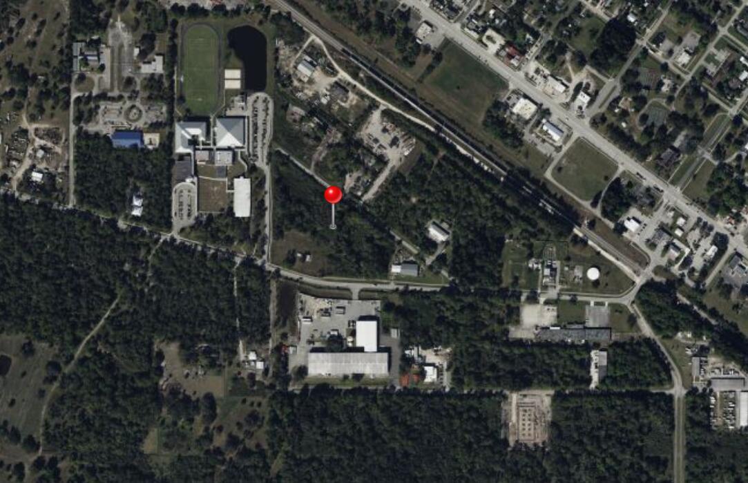 This aerial map shows a red location pin over a wooded lot near commercial buildings — 0 SW Carrier Street, FL 34956, FL