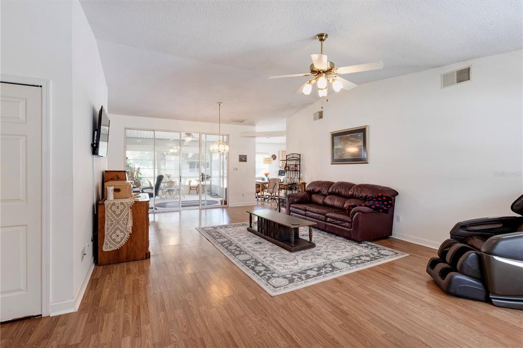 A living room features wood-look flooring, a brown leather sofa, and a ceiling fan — 5030 EL DESTINO DRIVE, LEESBURG, FL