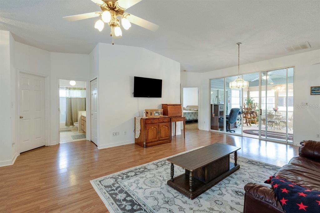 A living room with wood-look flooring, a ceiling fan, a television, and a glass-enclosed patio — 5030 EL DESTINO DRIVE, LEESBURG, FL