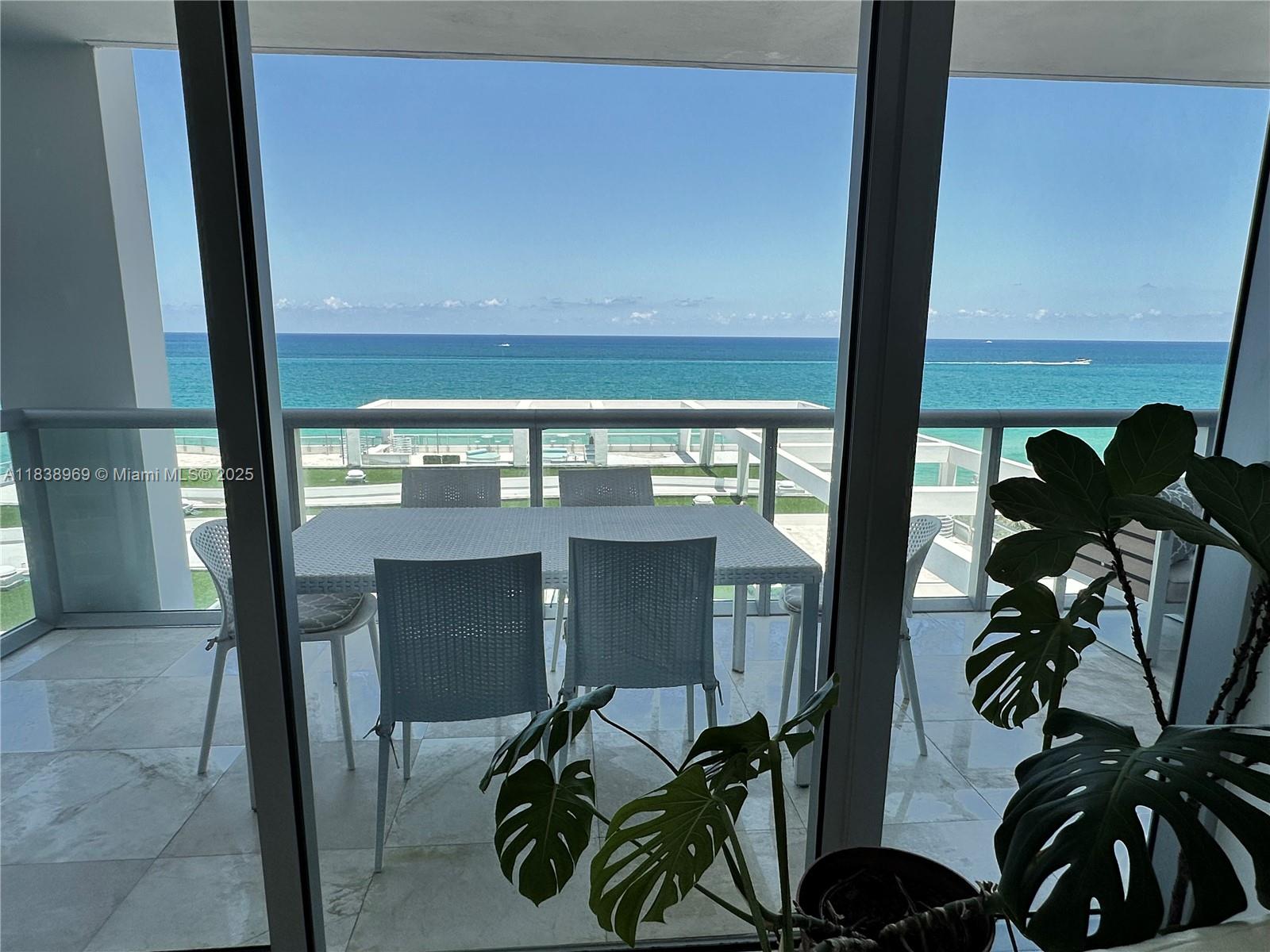A balcony with a dining set overlooks the ocean through large glass sliding doors — 6799 Collins Ave # 804, Miami Beach FL 33141, MIAMI BEACH, FL