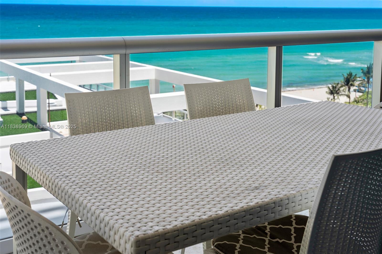 A balcony features a woven dining set overlooking the ocean and a white building — 6799 Collins Ave # 804, Miami Beach FL 33141, MIAMI BEACH, FL