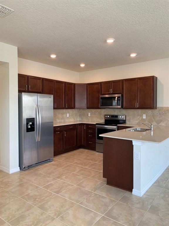 A kitchen with dark wood cabinets, stainless steel appliances, and light-colored countertops — 2101 GOPHER TORTOISE TERRACE, OAKLAND, FL