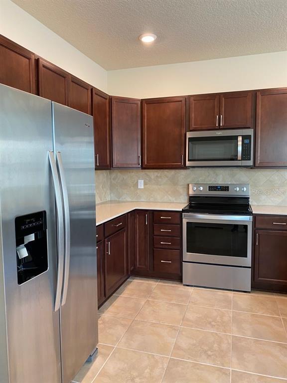 A kitchen features dark wood cabinets, stainless steel appliances, and light-colored tile flooring — 2101 GOPHER TORTOISE TERRACE, OAKLAND, FL