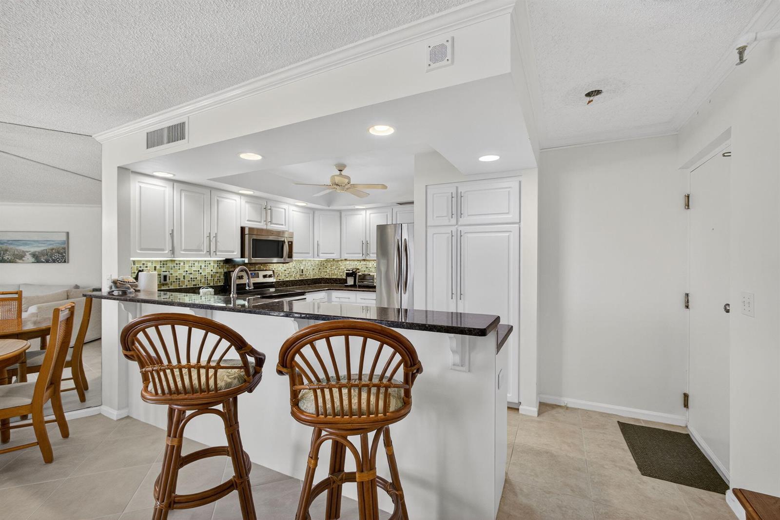 A kitchen with white cabinets, dark countertops, and two rattan bar stools at a counter — 2800 N Ocean Drive # 3a, Singer Island FL 33404, SINGER ISLAND, FL