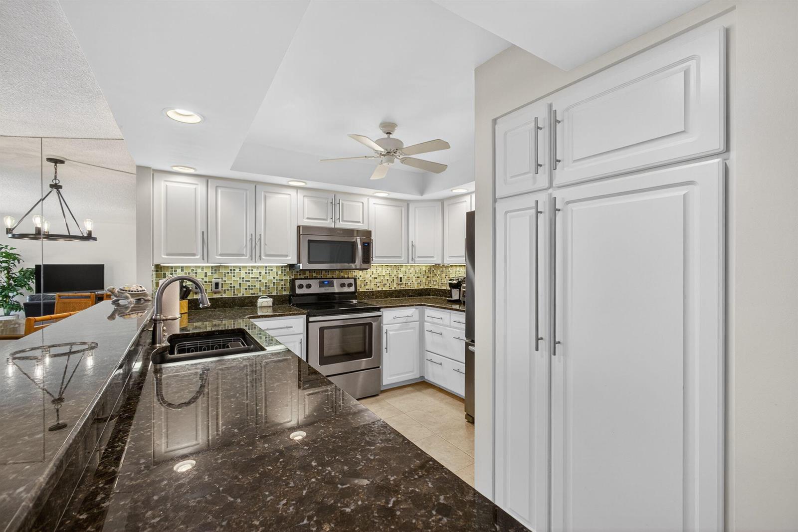 A kitchen features white cabinets, dark granite countertops, stainless steel appliances, and a tiled backsplash — 2800 N Ocean Drive # 3a, Singer Island FL 33404, SINGER ISLAND, FL