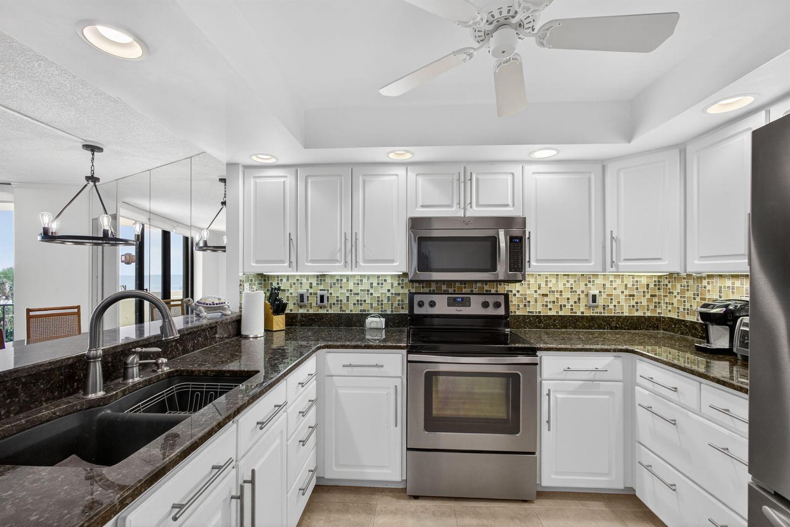 A kitchen features white cabinets, dark granite countertops, stainless steel appliances, and a mosaic backsplash — 2800 N Ocean Drive # 3a, Singer Island FL 33404, SINGER ISLAND, FL