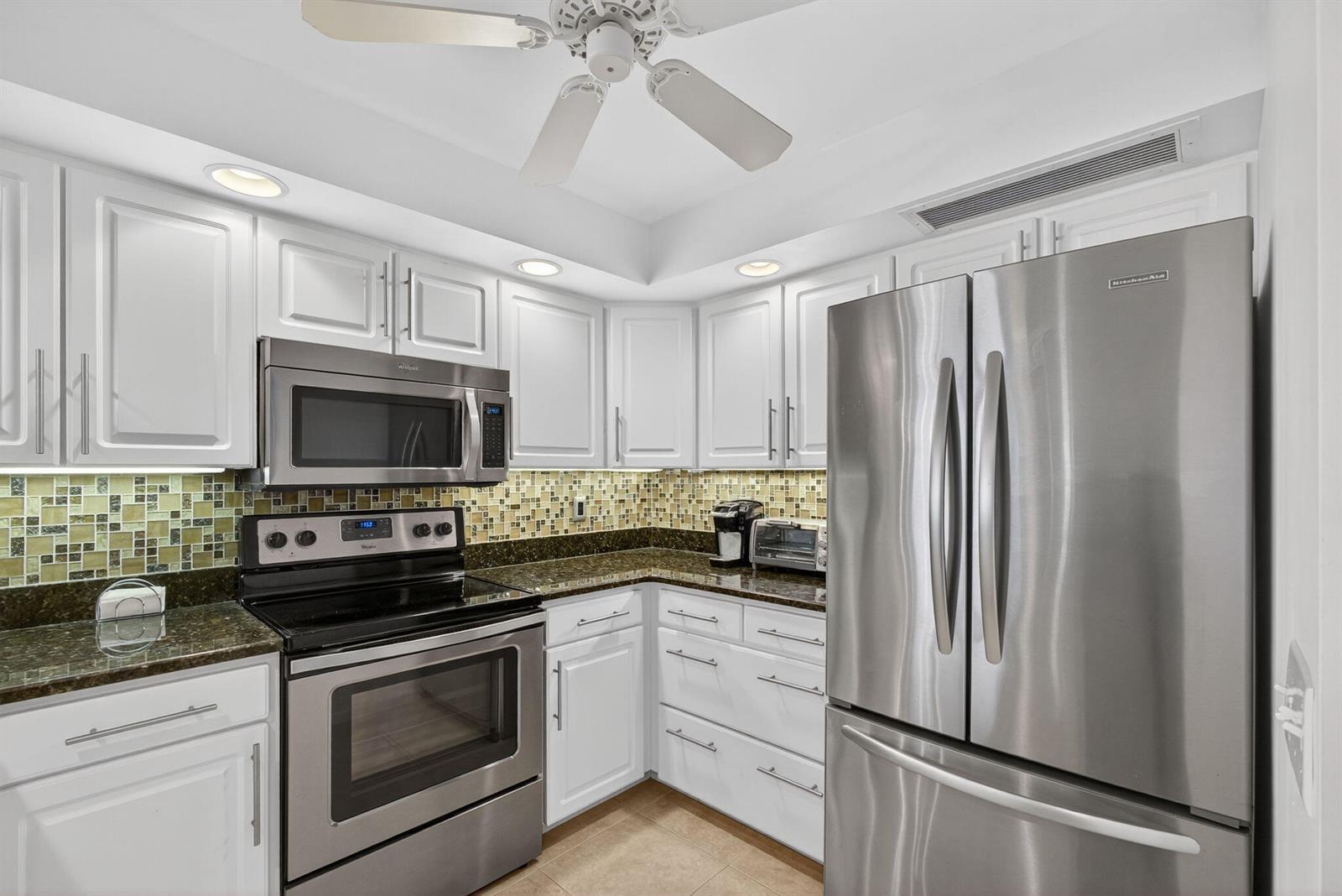 A kitchen features white cabinets, stainless steel appliances, a mosaic tile backsplash, and granite countertops — 2800 N Ocean Drive # 3a, Singer Island FL 33404, SINGER ISLAND, FL