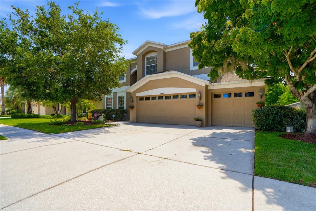 A two-story house with a tan exterior, a three-car garage, and mature trees in front — 9643 ASBEL ESTATES STREET, LAND O LAKES, FL