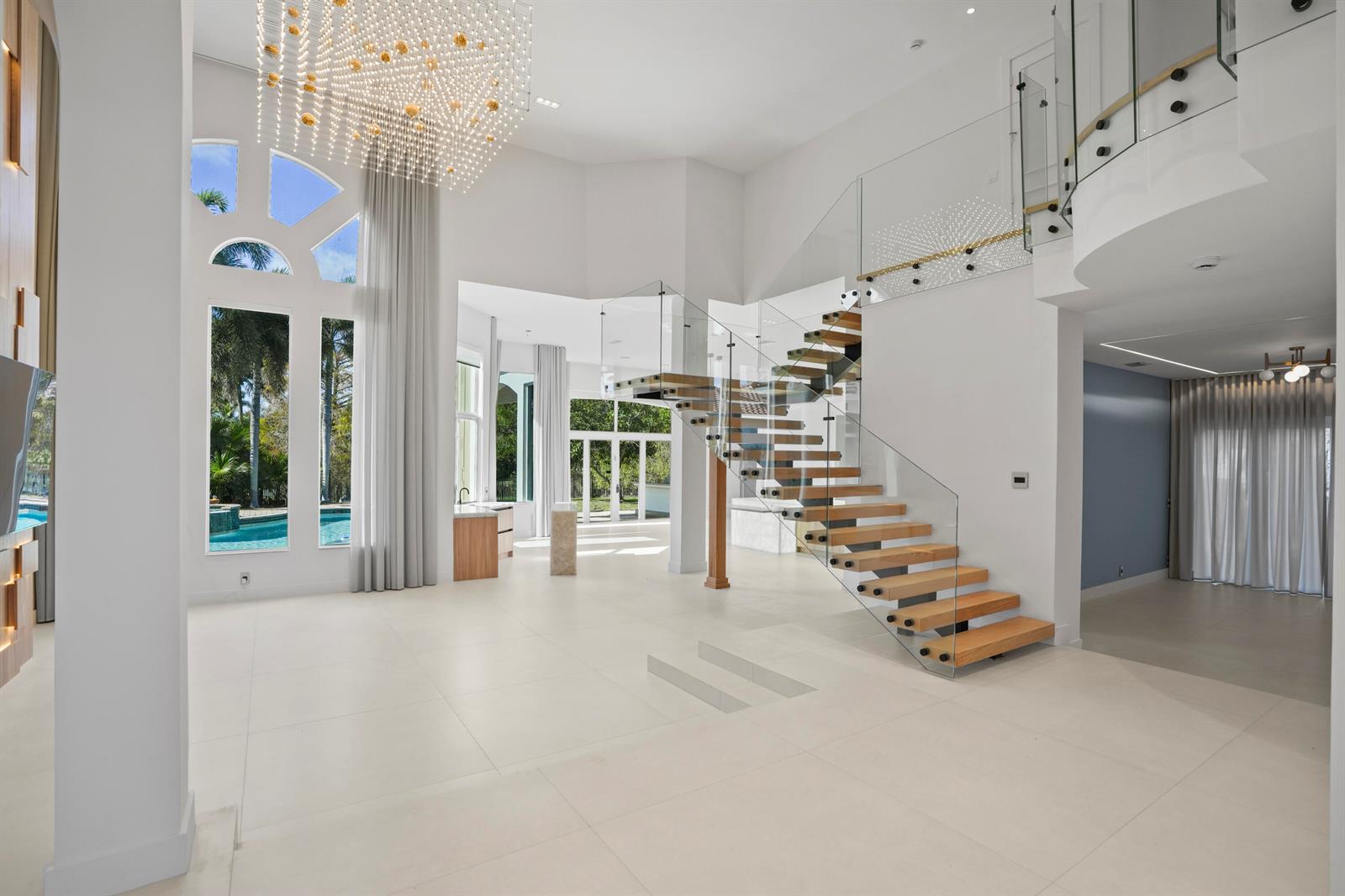 A bright, open-concept living area features a modern floating staircase, glass railings, and large windows — 3201 E Stonebrook Circle, Davie FL 33330, DAVIE, FL