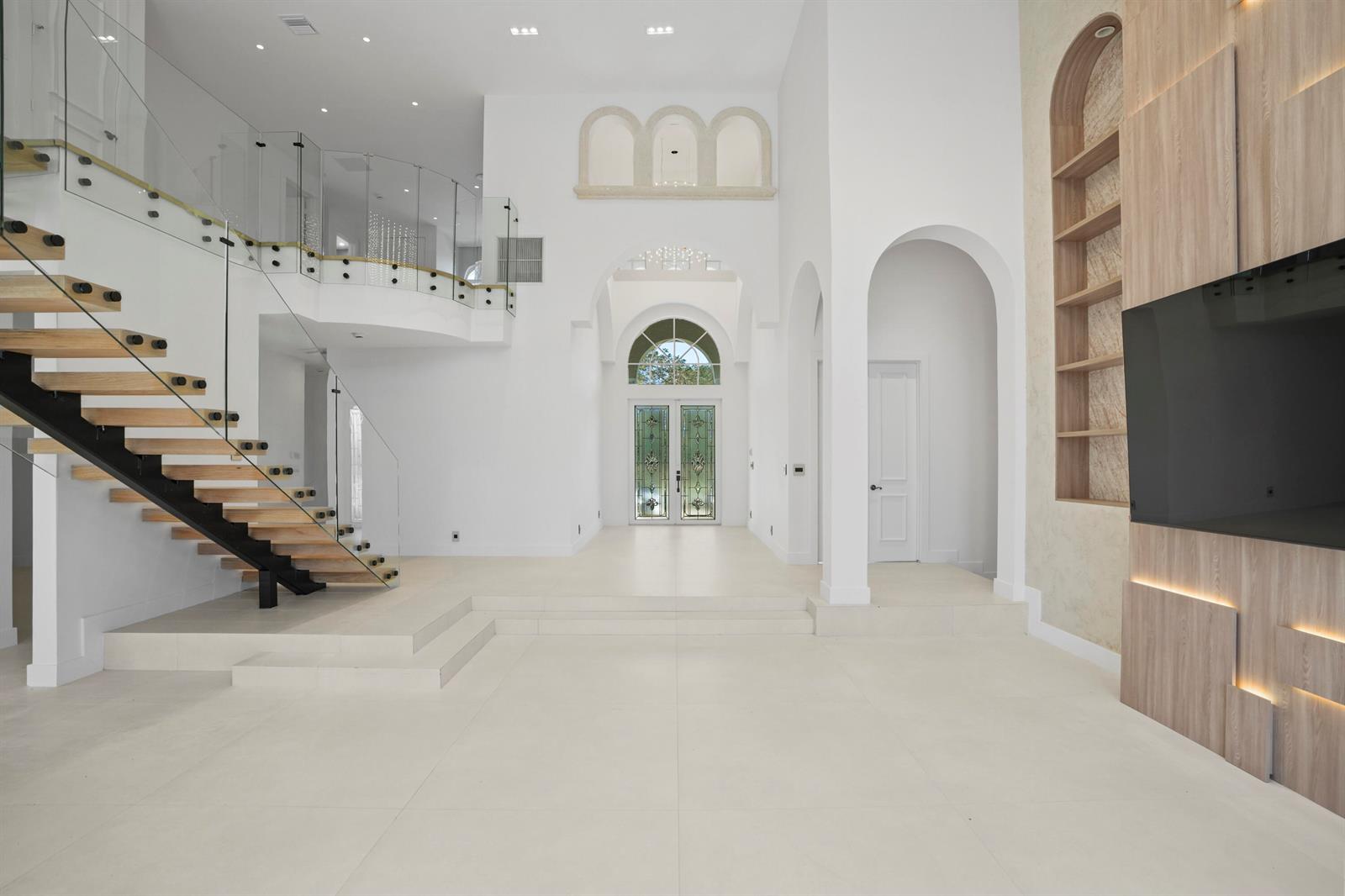 A bright, modern foyer features white tile floors, a floating staircase, and arched architectural details — 3201 E Stonebrook Circle, Davie FL 33330, DAVIE, FL