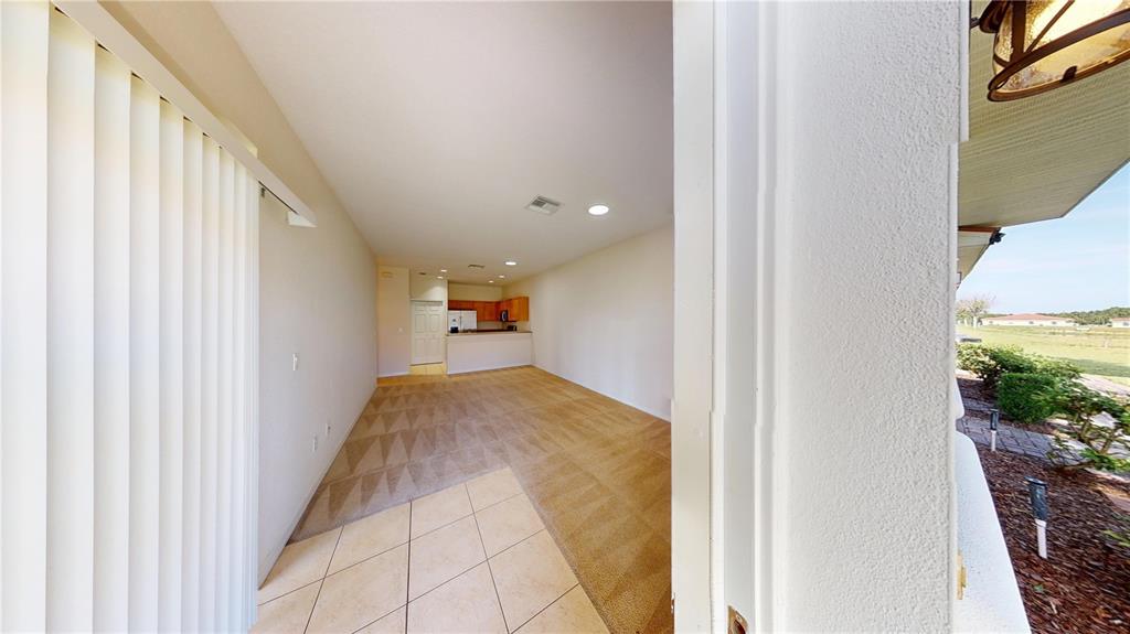 A view from a doorway looking into a carpeted living area with a distant kitchen — 1560 CUMIN DRIVE, KISSIMMEE, FL