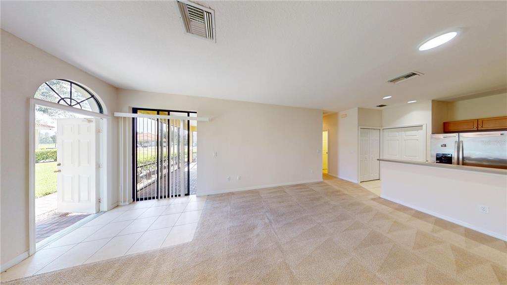 An open-concept living area features beige carpeting, tile flooring, and a sliding glass door — 1560 CUMIN DRIVE, KISSIMMEE, FL