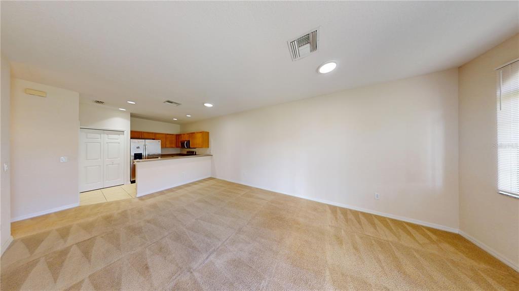 An open-concept living room features beige carpeting, neutral walls, and an adjacent kitchen area — 1560 CUMIN DRIVE, KISSIMMEE, FL