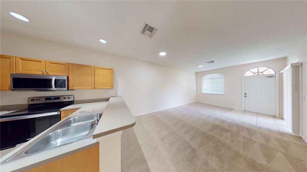 A kitchen with light wood cabinets and a breakfast bar overlooks a carpeted living area — 1560 CUMIN DRIVE, KISSIMMEE, FL