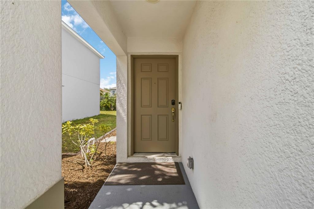 A tan front door with six panels is set within a covered entryway — 7148 CHATUM LIGHT RUN, BRADENTON, FL