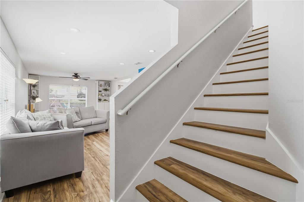 A staircase with wood treads and white risers leads up beside a living room — 7148 CHATUM LIGHT RUN, BRADENTON, FL