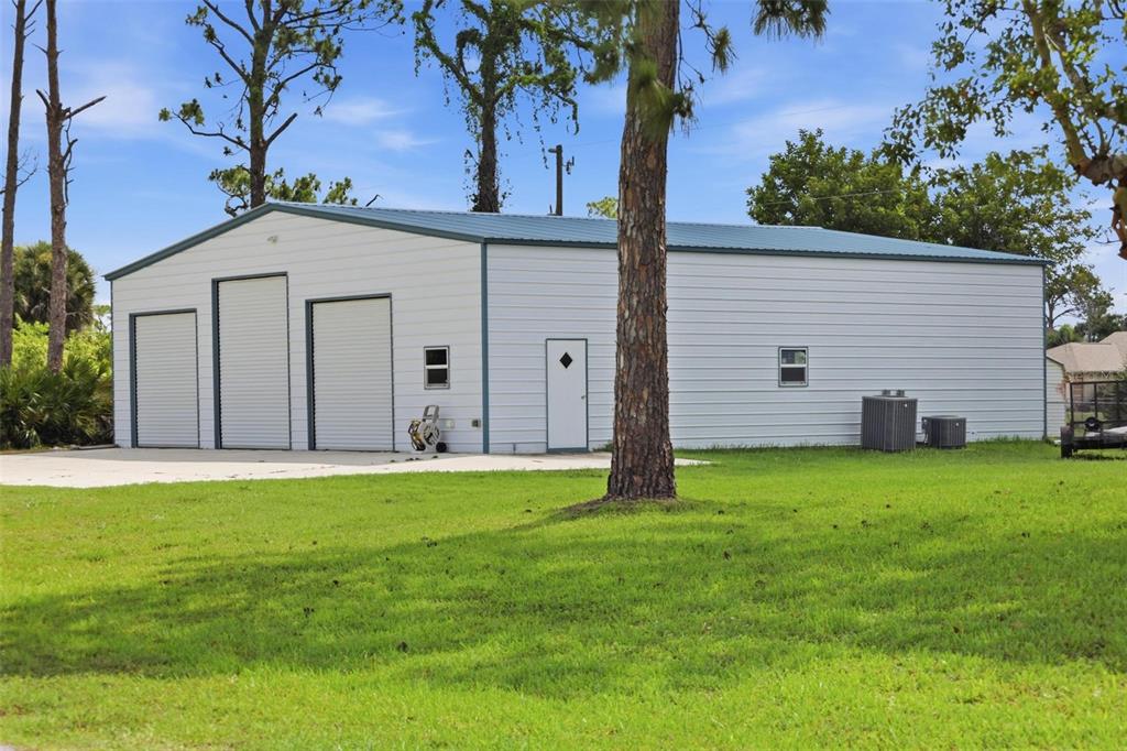 A white metal workshop building with three garage doors and a side entry door — 5412 ULYSSES STREET, PORT CHARLOTTE, FL
