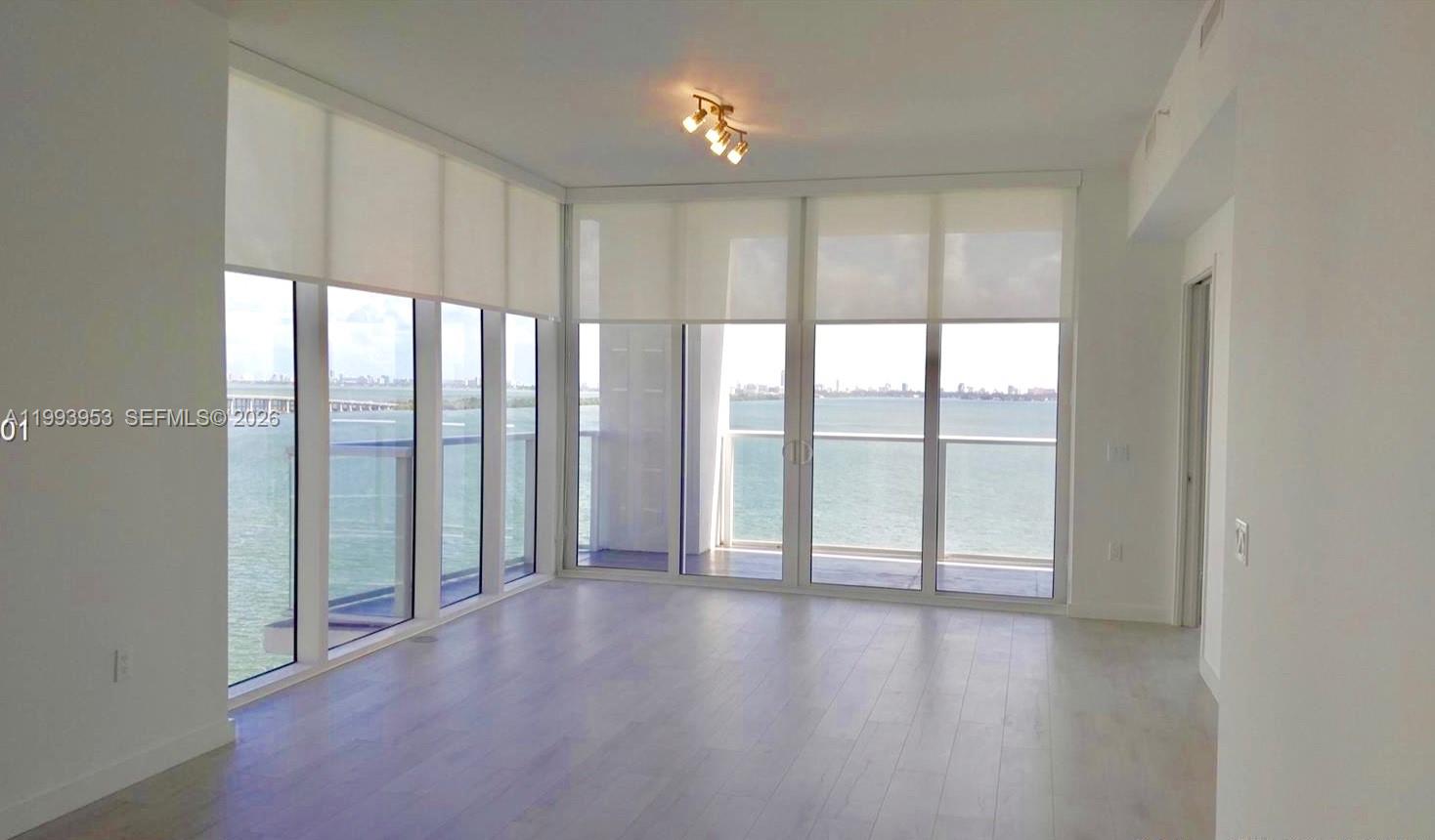 An empty room features light wood flooring, floor-to-ceiling windows, and a balcony overlooking water — 601 NE 27TH ST # 1107, Miami FL 33137, MIAMI, FL