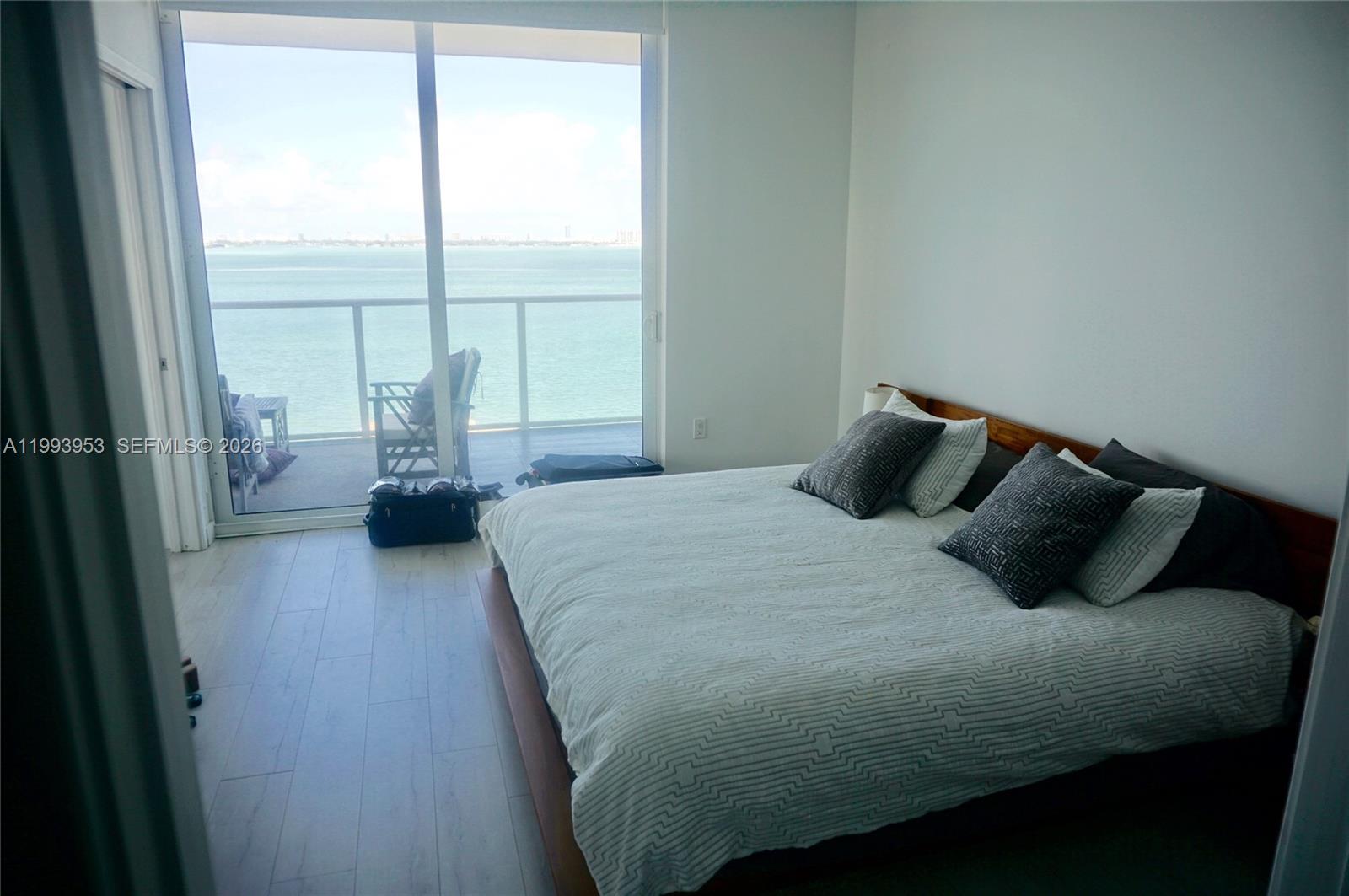 A bedroom features a platform bed, light wood-look flooring, and a balcony overlooking the water — 601 NE 27TH ST # 1107, Miami FL 33137, MIAMI, FL