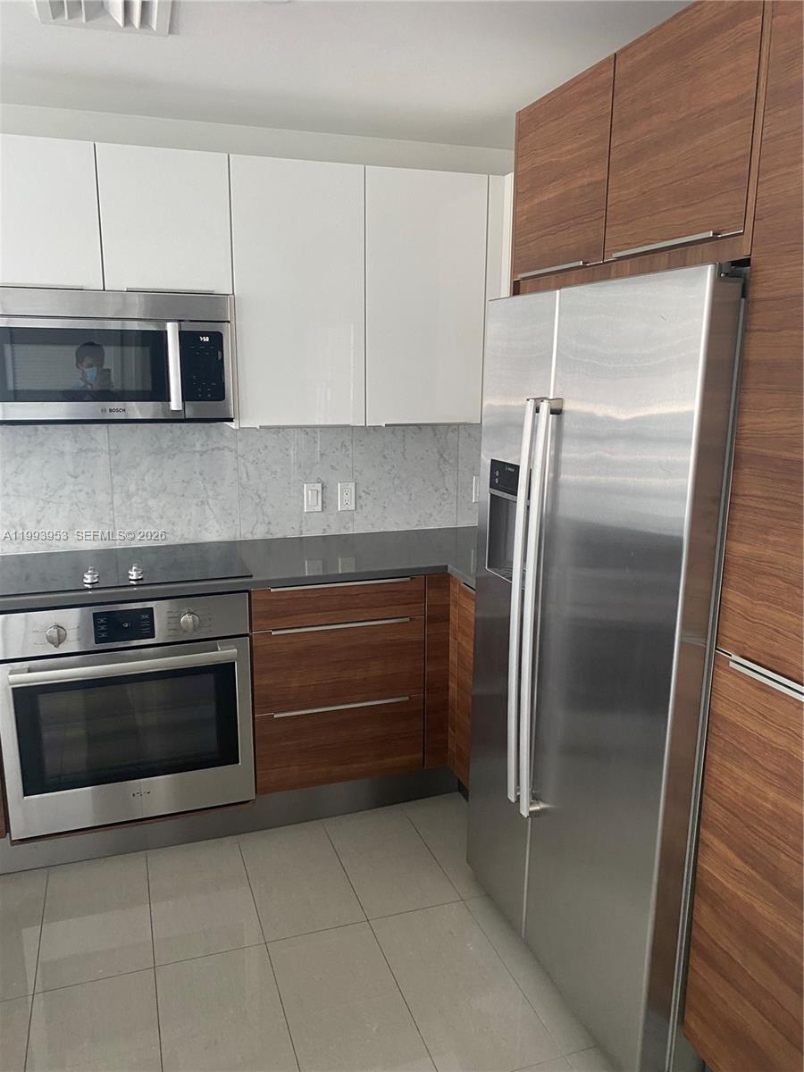 A modern kitchen features white upper cabinets, wood-grain lower cabinets, and stainless steel appliances — 601 NE 27TH ST # 1107, Miami FL 33137, MIAMI, FL