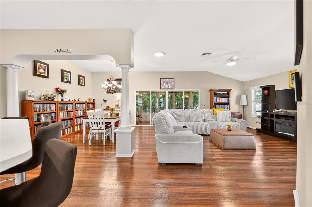 A spacious open-concept living and dining area features wood flooring, a sectional sofa, and bookshelves — 16767 SE 77TH NORTHRIDGE COURT, THE VILLAGES, FL