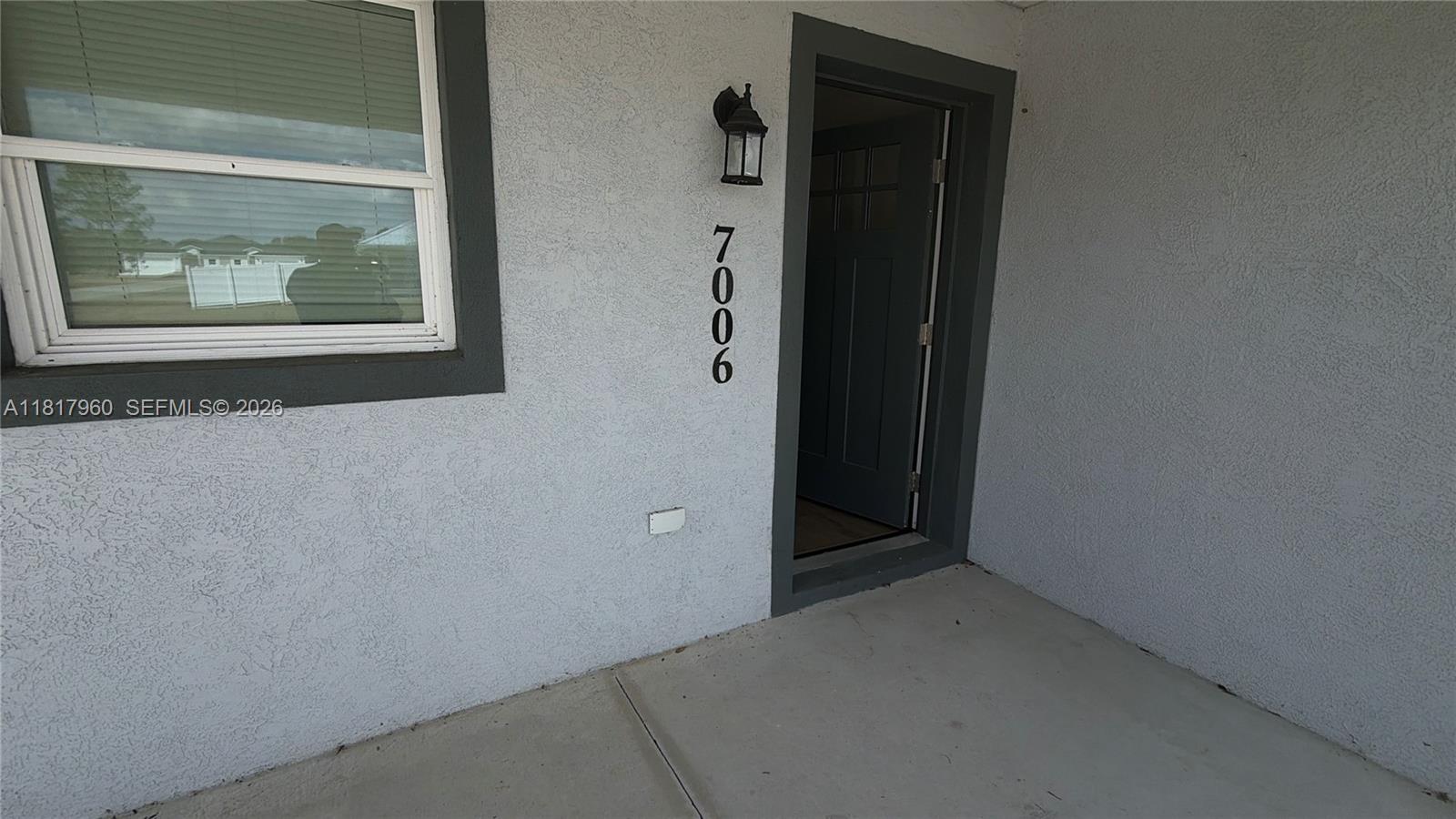 A gray stucco exterior wall features a window, a dark front door, and house number 7006 — 7006 San Bruno Dr, Sebring FL 33872, SEBRING, FL