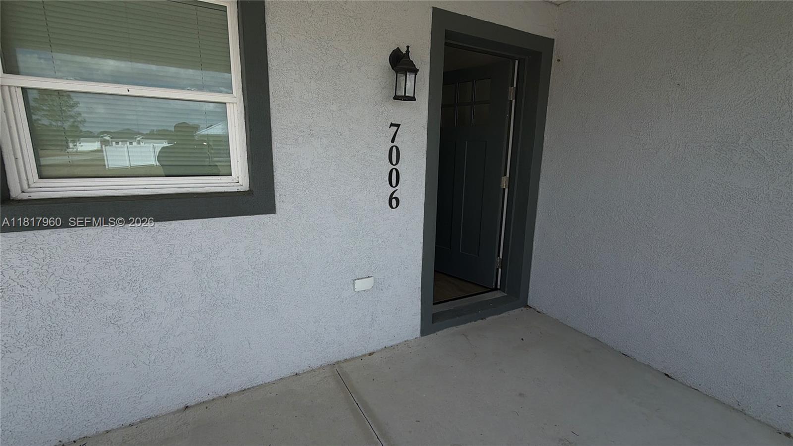 This exterior view shows a gray stucco wall with a window, a door, and house numbers — 7006 San Bruno Dr, Sebring FL 33872, SEBRING, FL