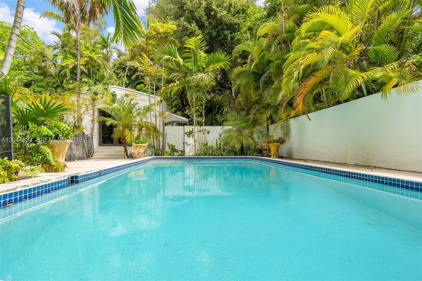 A rectangular swimming pool is surrounded by a white wall and lush tropical palm trees — 5390 Sunset Dr, Miami FL 33143, MIAMI, FL