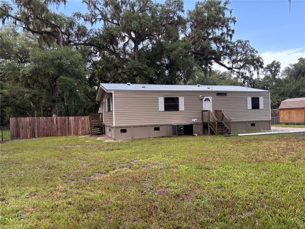 A single-story manufactured home with tan siding sits on a grassy lot with trees — 16581 NE 42ND AVENUE, CITRA, FL