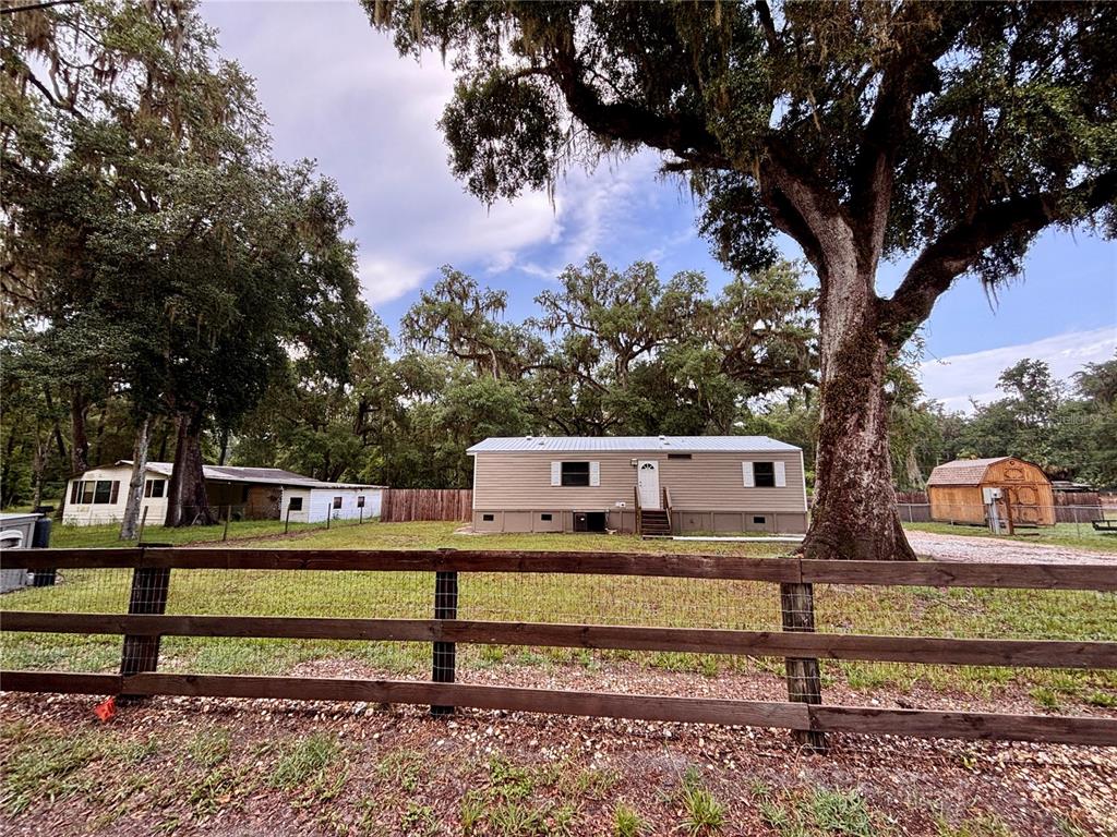 A tan mobile home sits on a grassy lot behind a wooden fence with trees — 16581 NE 42ND AVENUE, CITRA, FL