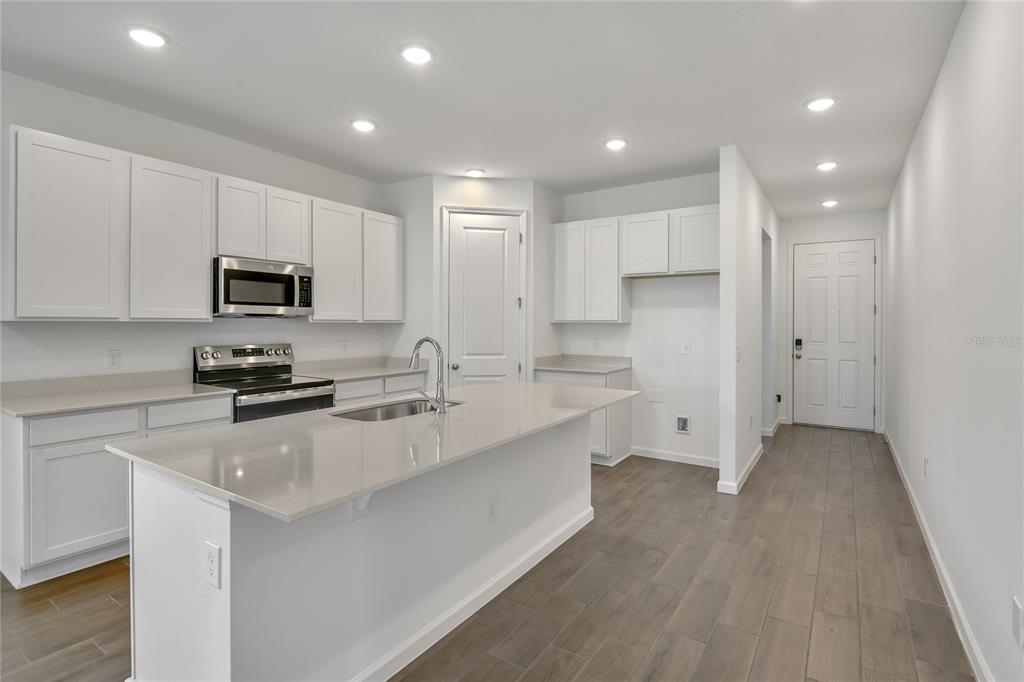 A modern kitchen features white cabinets, stainless steel appliances, a quartz island, and wood-look flooring — 5147 KINSLEY DRIVE, WINTER HAVEN, FL