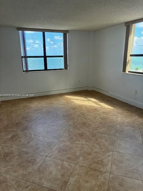 An empty room features tan tile flooring and large windows with a view of the ocean — 10185 Collins Ave # 917, Bal Harbour FL 33154, BAL HARBOUR, FL