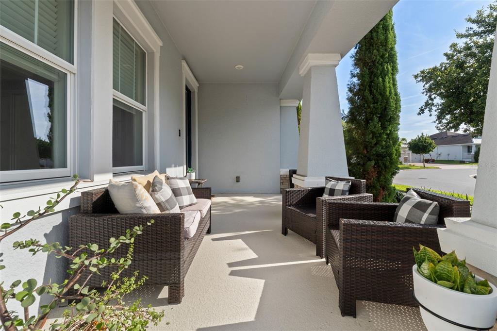 A covered front porch features wicker furniture, light-colored concrete flooring, and white support columns — 14807 WINTER STAY DRIVE, WINTER GARDEN, FL