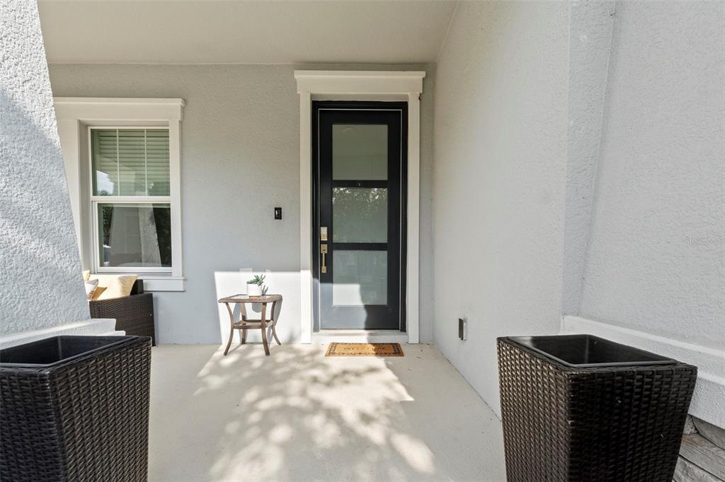 A covered front porch features a dark door with glass panels and two wicker planters — 14807 WINTER STAY DRIVE, WINTER GARDEN, FL