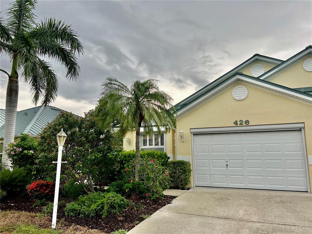A yellow house with a white garage door and palm trees under a cloudy sky — 426 GASPAR KEY LANE, PUNTA GORDA, FL