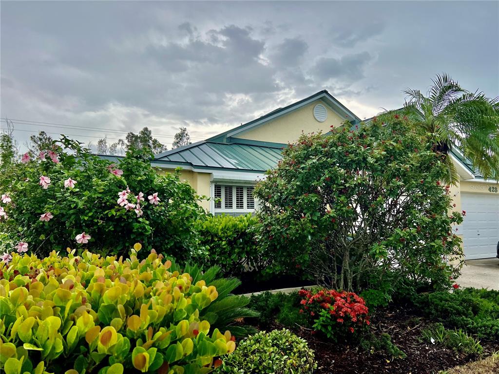 A single-story house with a green metal roof is surrounded by lush landscaping and flowers — 426 GASPAR KEY LANE, PUNTA GORDA, FL