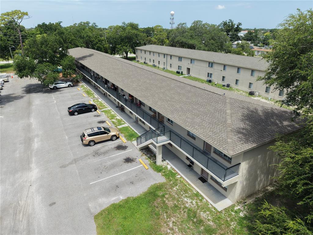 An aerial view shows two long, multi-story apartment buildings with parking lots and surrounding trees — 6450 78TH AVENUE N UNIT 38, PINELLAS PARK, FL