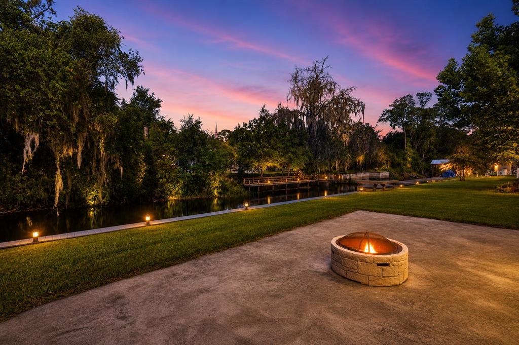 A stone fire pit sits on a concrete patio overlooking a grassy lawn and canal — 1330 S SHORE DRIVE, ST CLOUD, FL